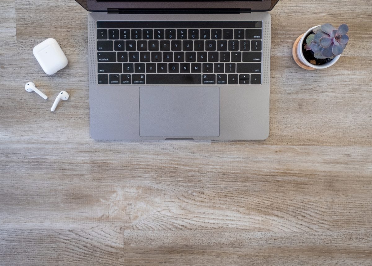MacBook mit AirPods und Sukkulente auf Holztisch, Blick von oben