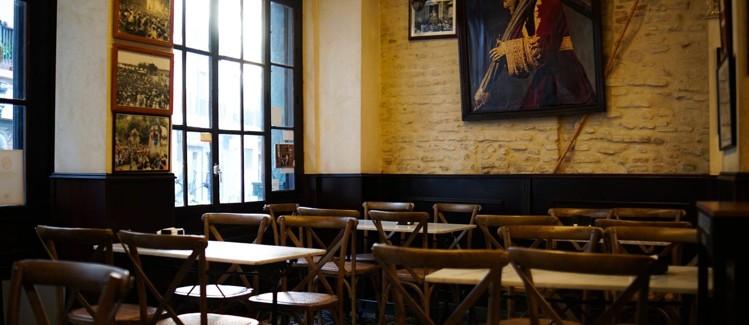 Blick in unser Café — Holztische, warmes Licht, Backsteinwand